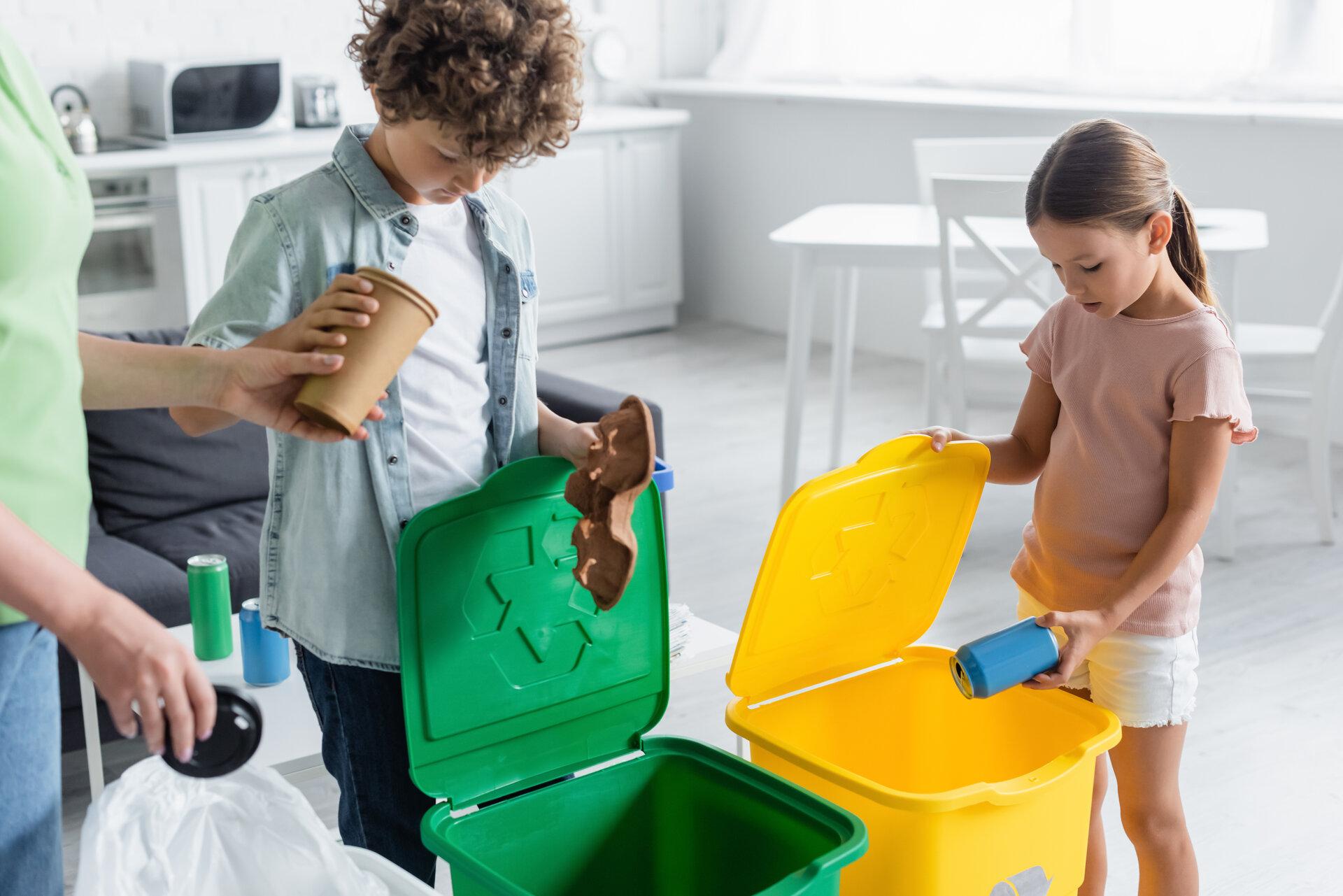 Kinder mit Mutter sortieren Müll in Mülleimern mit Recycling-Schild zu Hause.