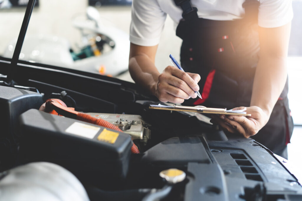 Auto-Check-up, Mechaniker, der eine Job-Checkliste in die Zwischenablage schreibt, um dem Kunden in der Werkstatt einen Kostenvoranschlag für die Reparatur zu machen