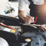 Auto-Check-up, Mechaniker, der eine Job-Checkliste in die Zwischenablage schreibt, um dem Kunden in der Werkstatt einen Kostenvoranschlag für die Reparatur zu machen