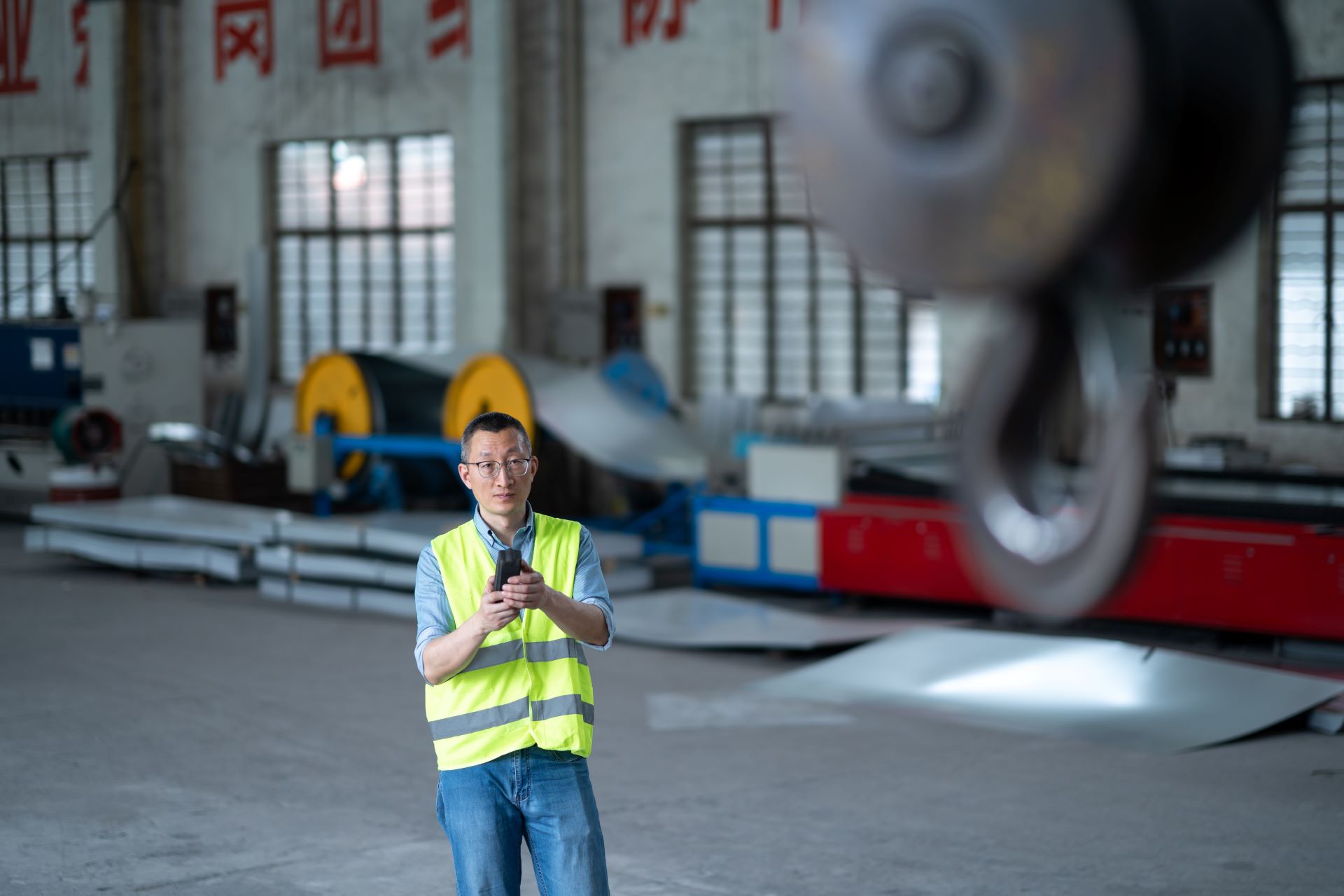 Arbeiter steuert Elektrokettenzug in einer großen Industriehalle.