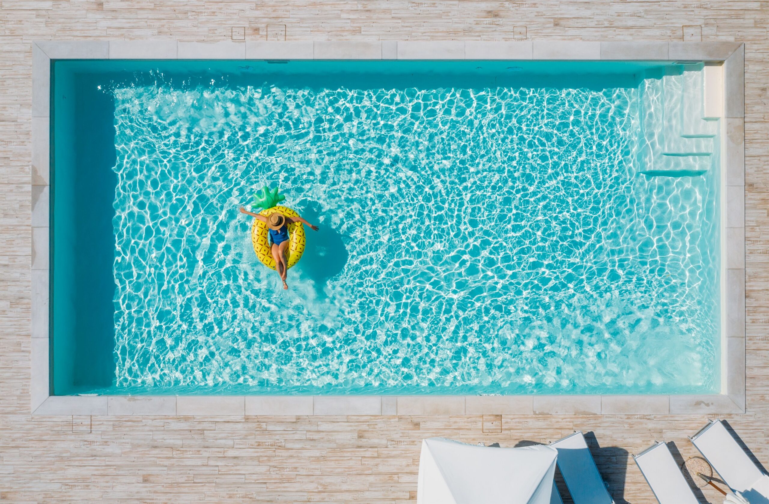 GFK Pool von oben mit klarer Wasserstruktur, rechteckiger Form und Treppeneinstieg, Frau entspannt auf Schwimmring
