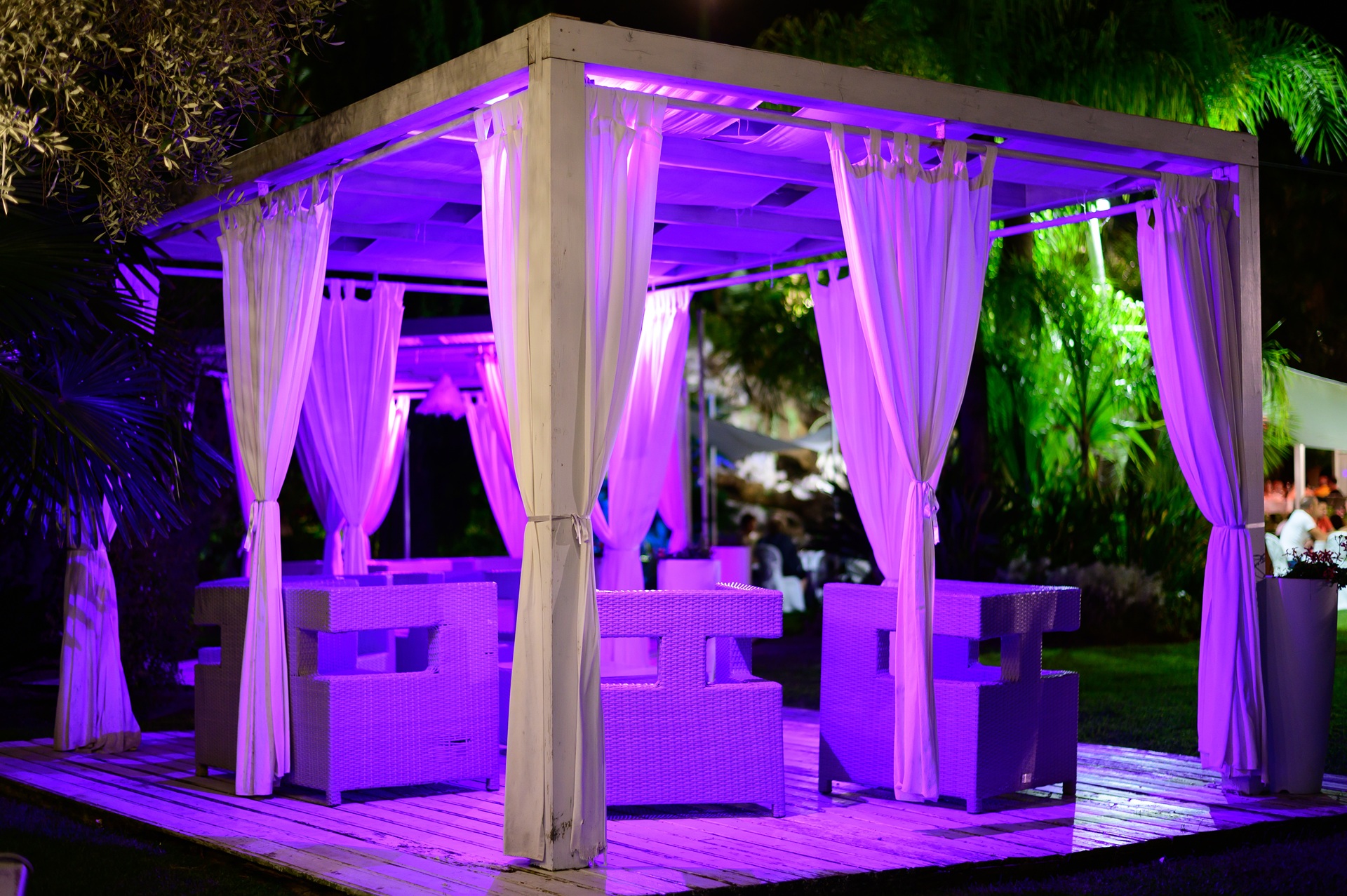 Beleuchtete Cabana mit weissen Vorhängen und lila Licht | Kaminholzregal Metall außen